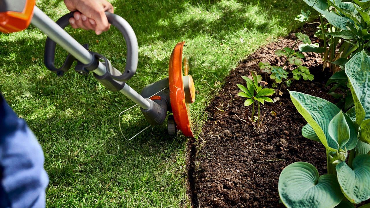 Automower sitting in grass patch in backyard with family cooking bbq in background